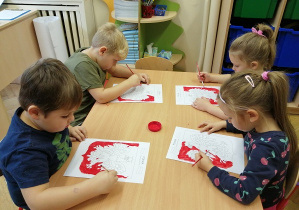 dzieci przy stoliku malują godło farbami